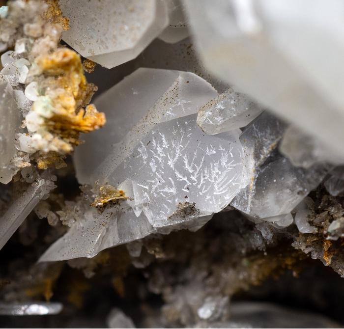 Скелетный рост кристаллов гипса на поверхности кристалла серого кальцита. Кальцит находится среди кристаллов белого и оранжевого кварца. Поле зрения 3 см. Фотография Бадьяновой Л. В