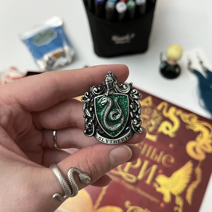 Значок факультета Слизерин. Жаль я не сфотографировала подарки в упаковке. Потому что этот подарок был упакован в бумагу и подписан «Настоящему гриффиндорцу». Я такая «Чтоооооо?» А потом как поняла! 😃