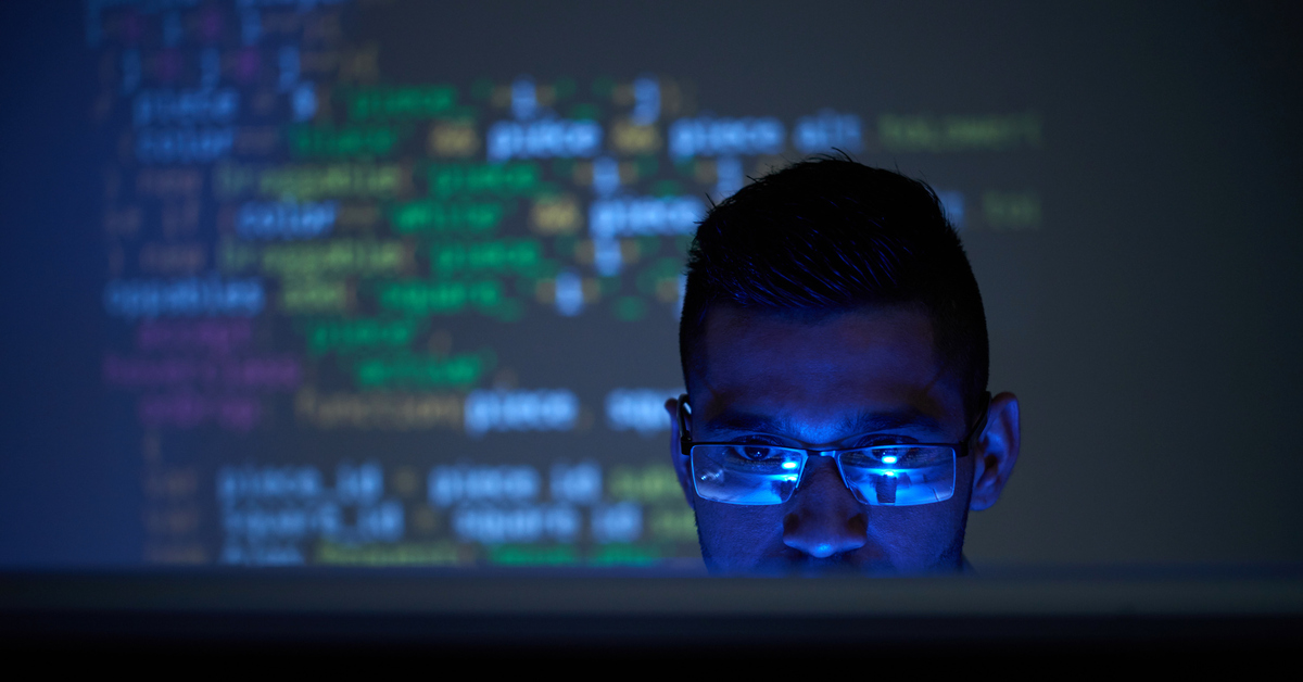 мужчина в очках смотрит на код на экране монитора